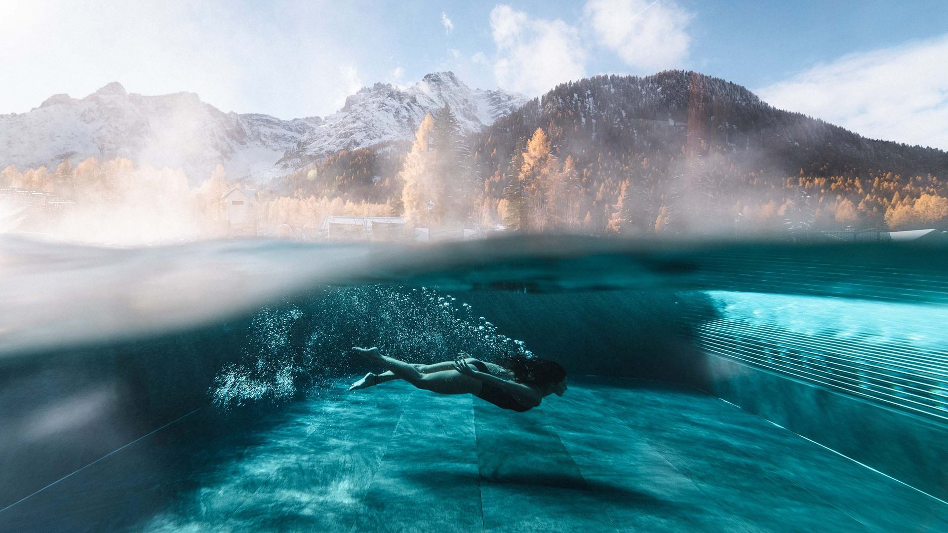 Zinnit Destinations | Drei Zinnen Dolomiten Taucher unter Wasser in Pool vor bergiger Landschaft mit Schnee und Herbstbäumen